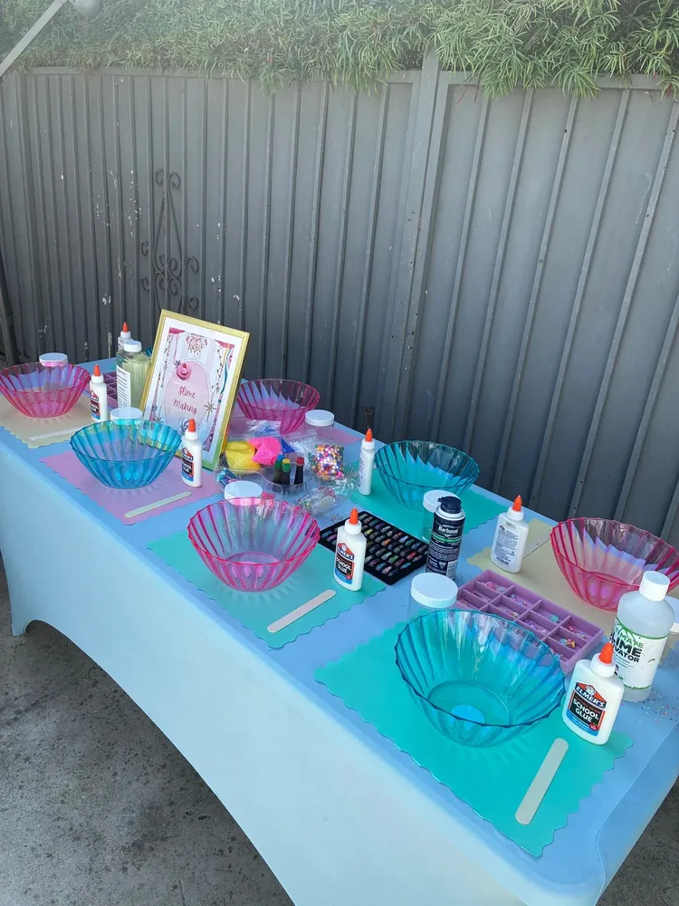 Colorful bowls, glue, and supplies arranged at a slime-making station.