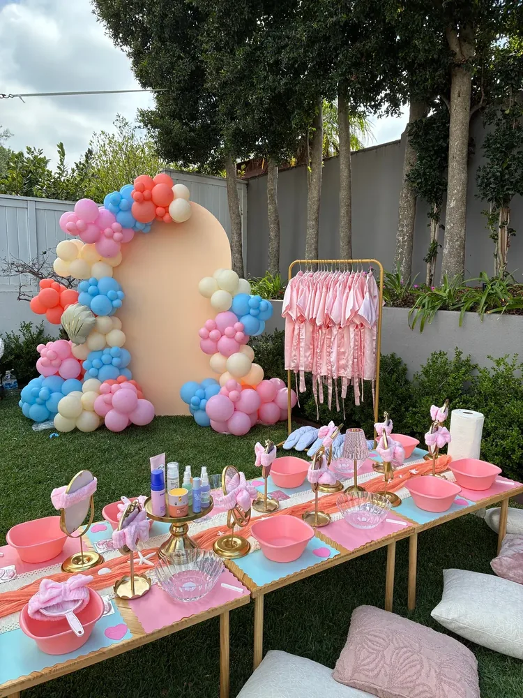 Outdoor setup with a balloon arch, robe rack, and spa activity table.