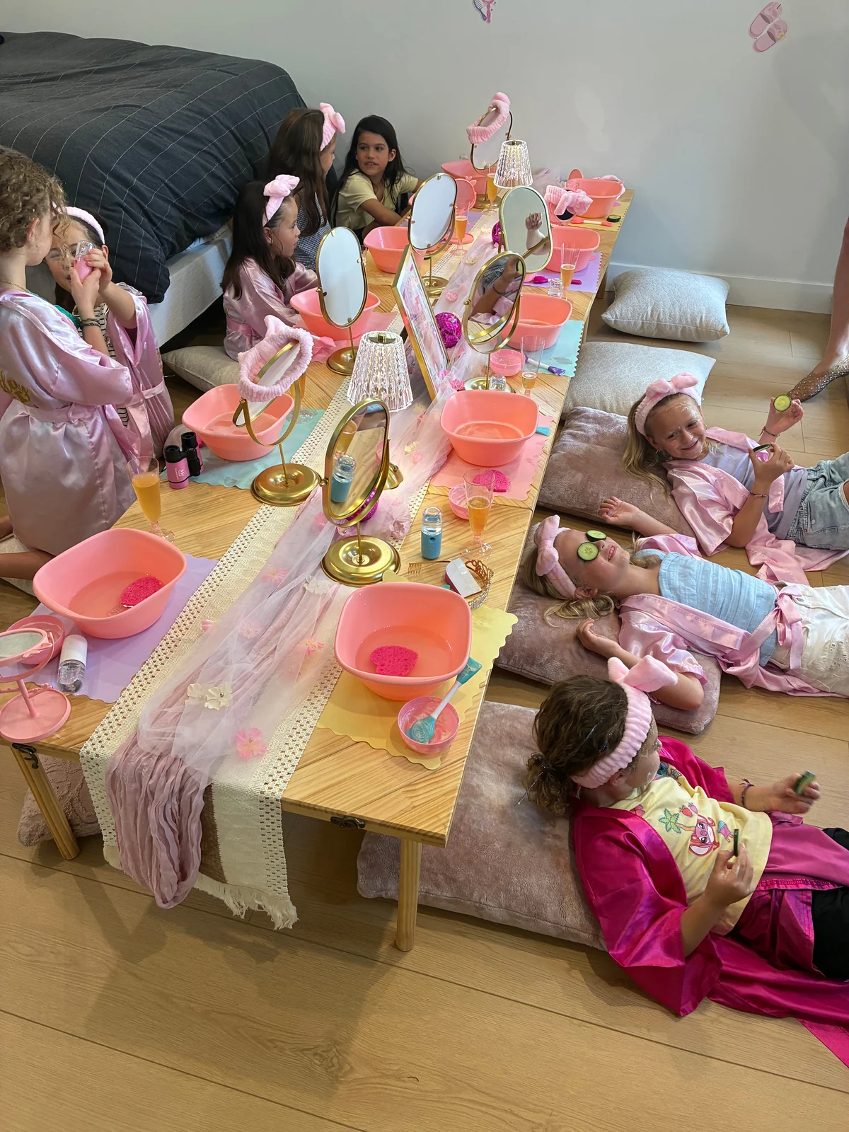 Children in pink spa robes gather at a table of spa supplies.