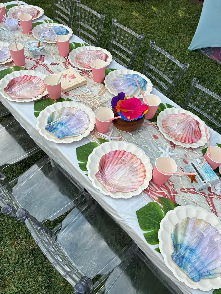 Shell-shaped plates and pink cups arranged at an outdoor table.