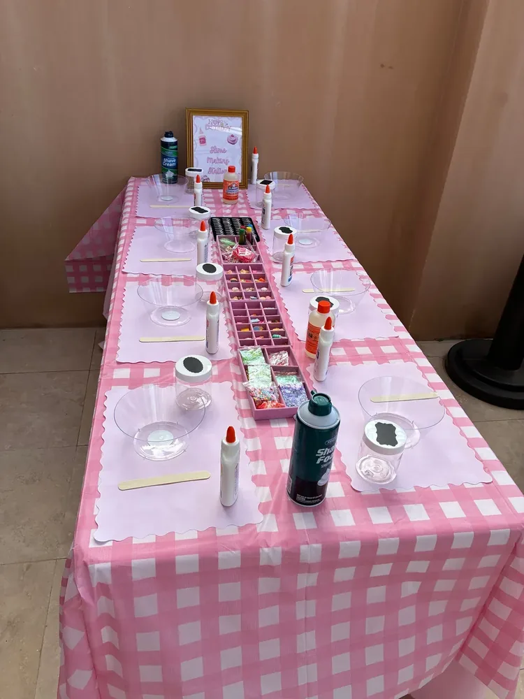 A pink craft table set with squeeze bottles, bowls, beads, and supplies.