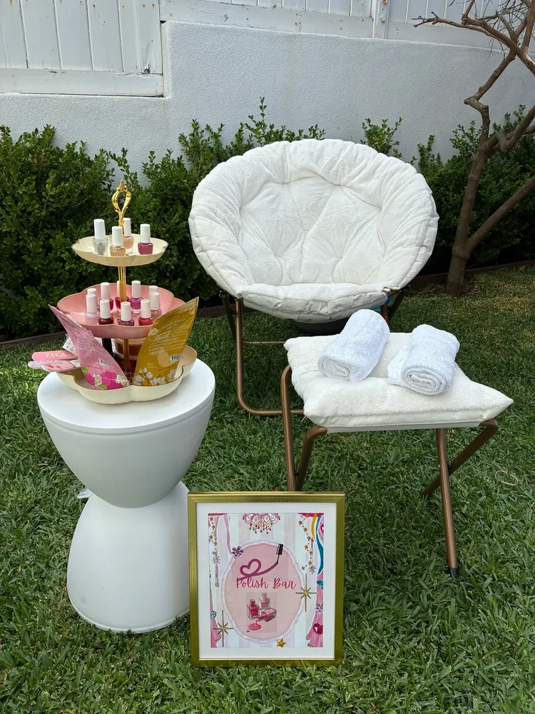 A white lounge chair beside a pink manicure table and spa-party sign.